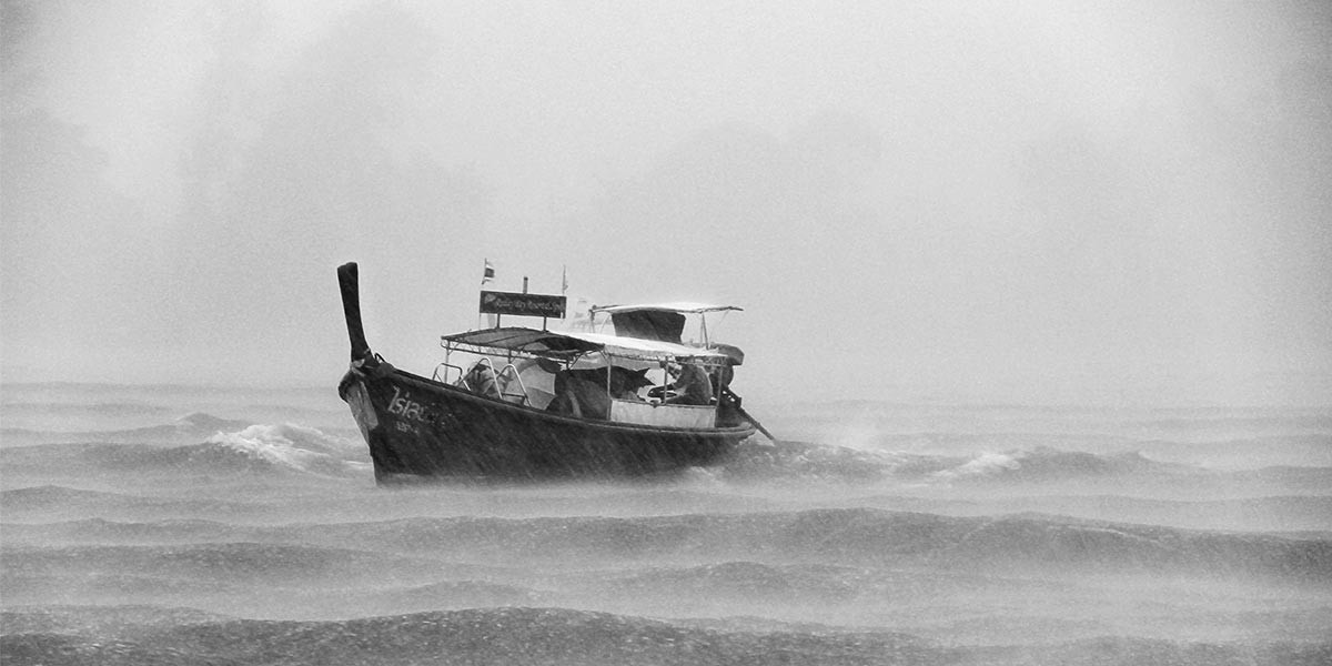Small boat navigating rough seas amid heavy rain and mist in grayscale image.