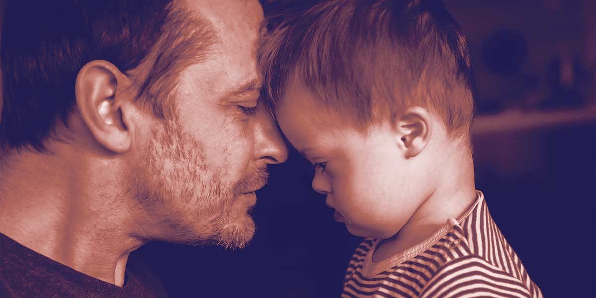 Man and child with Down syndrome touching foreheads with closed eyes in a tender moment.