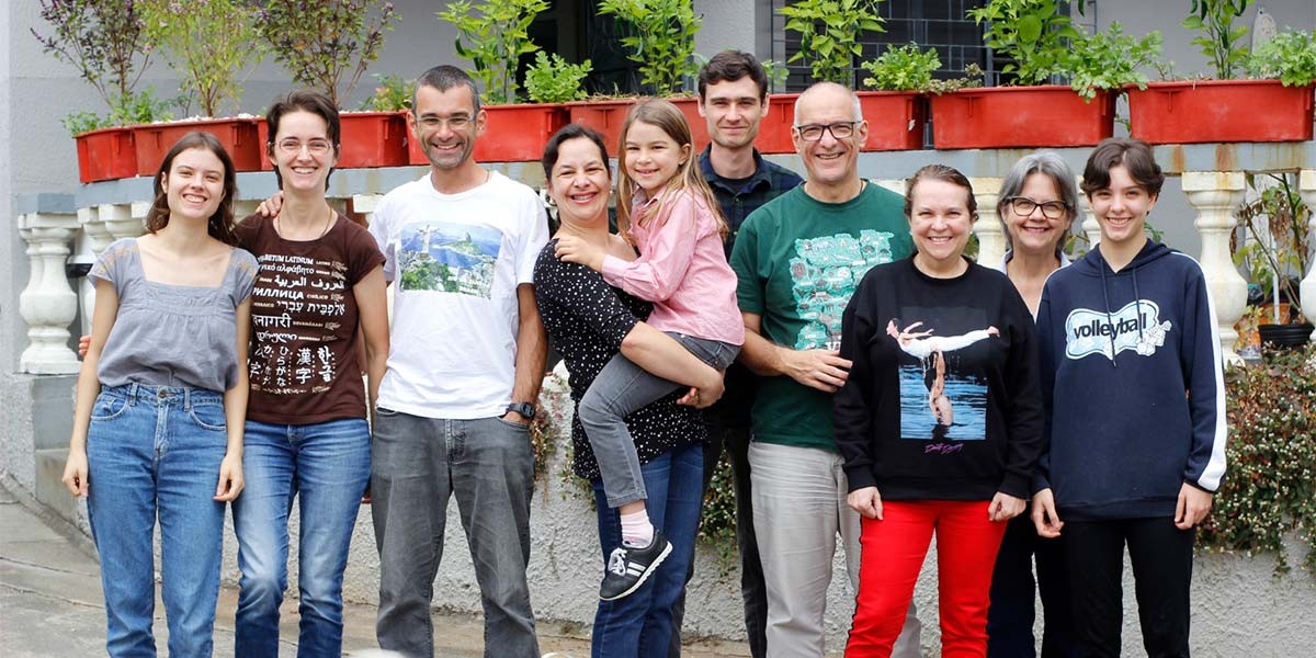 Group of eleven people, including adults and children, standing together outside with plants behind them.