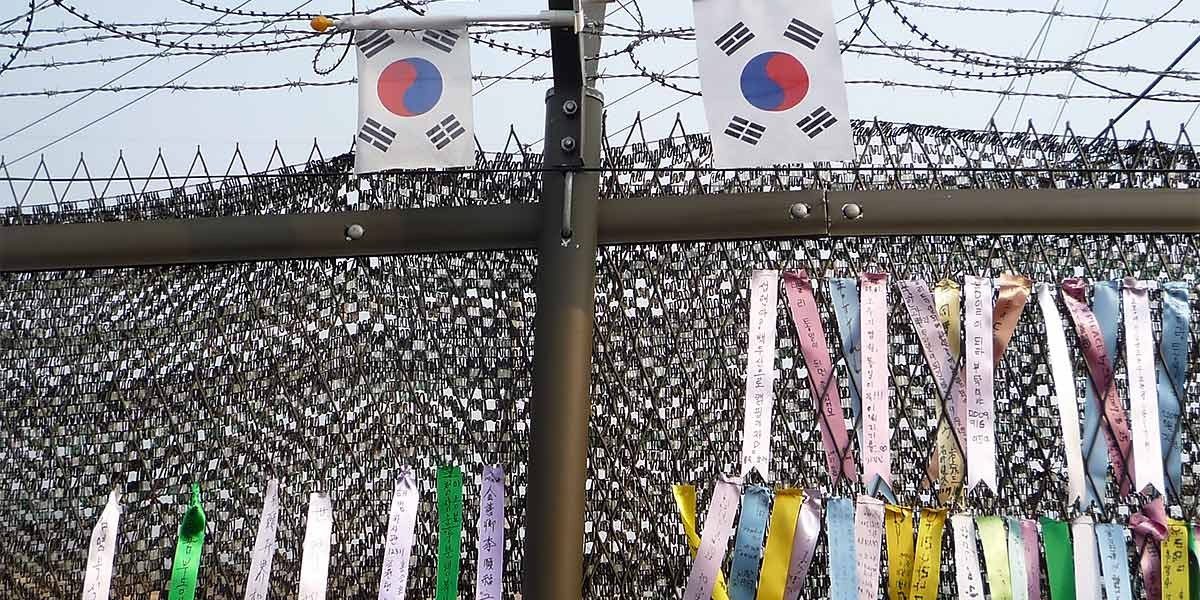 Barbed wire fence with colorful ribbons and two South Korean flags attached on top.