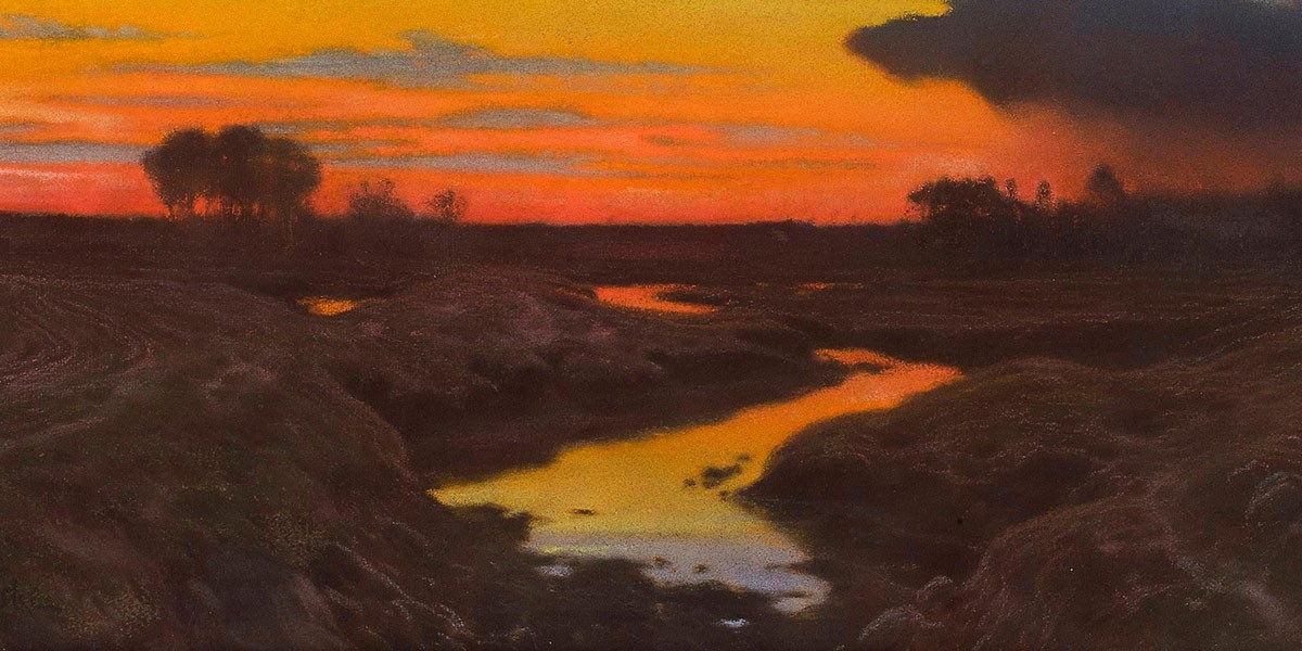 Orange and red sunset over a dark river landscape with silhouetted trees and clouds.