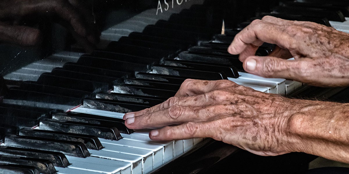 Close-up of elderly hands playing worn piano keys on a black piano.