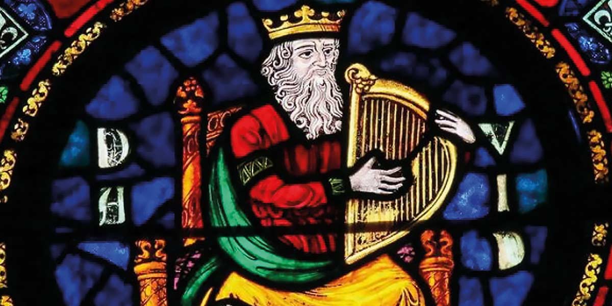 Stained glass window showing a bearded king playing a golden harp while seated on a throne.
