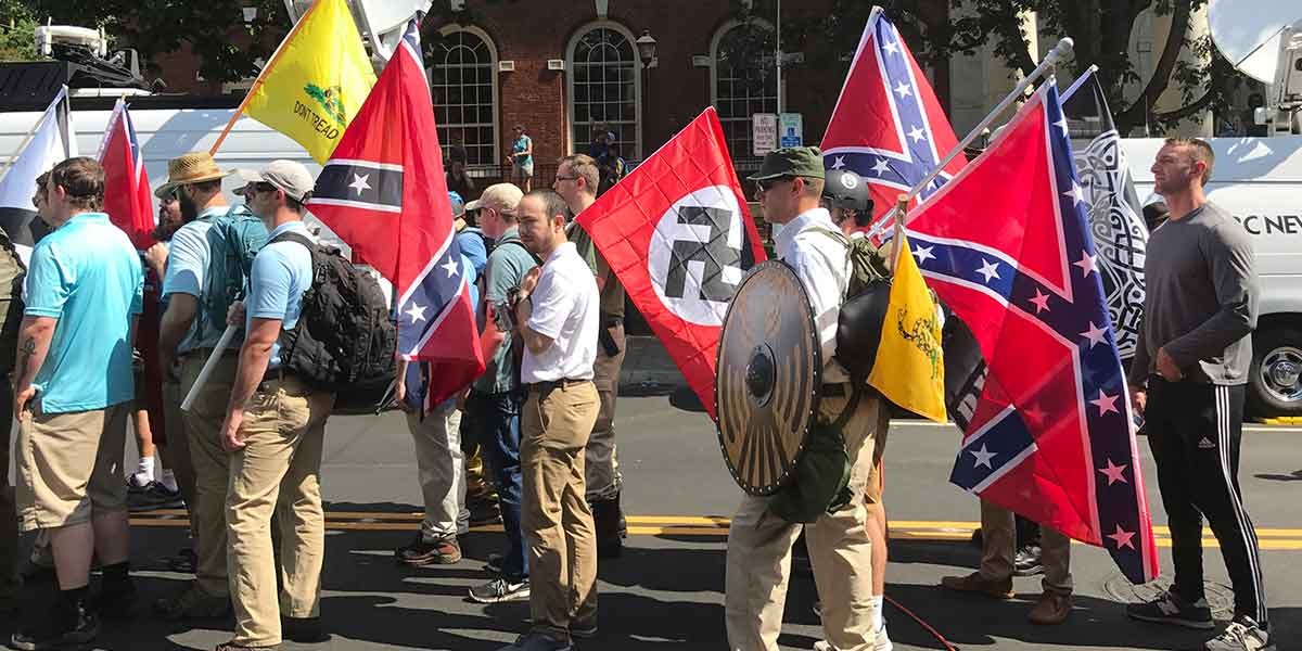 Group of men standing with flags including Confederate and Gadsden flags on a city street.