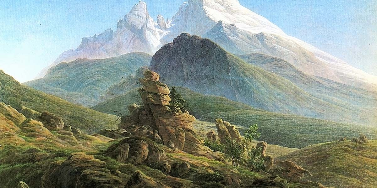 Mountain landscape with rocky outcrops and green foothills under a clear blue sky.