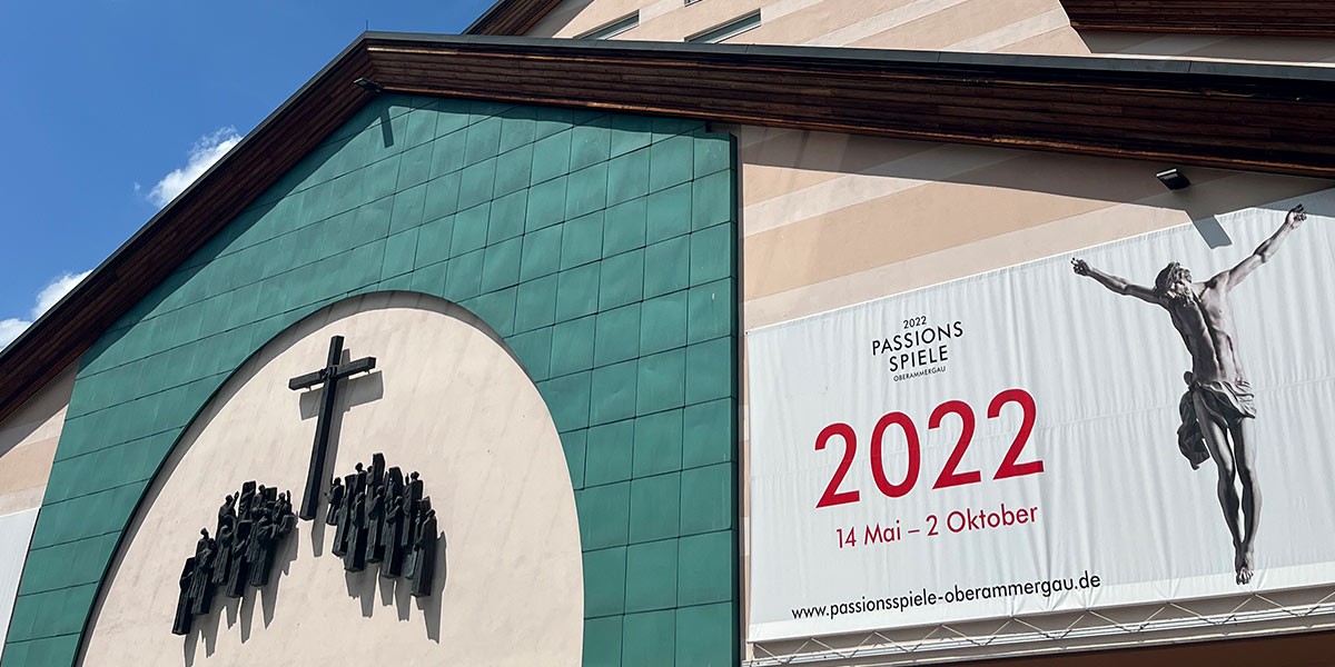 Building facade with cross, figures, and banner for 2022 Passionsspiele Oberammergau event dates.