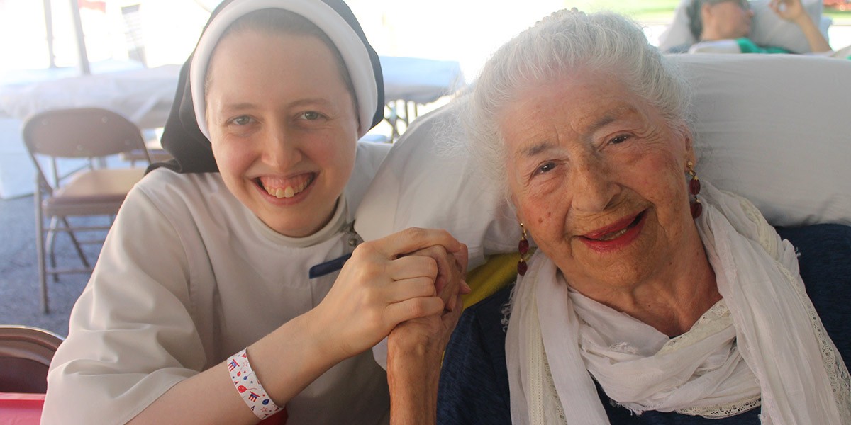 Smiling nun holding hands with an elderly woman, both looking happy and seated close together.