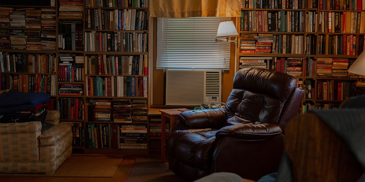 Cozy room with leather armchair, beige sofa, wooden side table, and bookshelves filled with books.