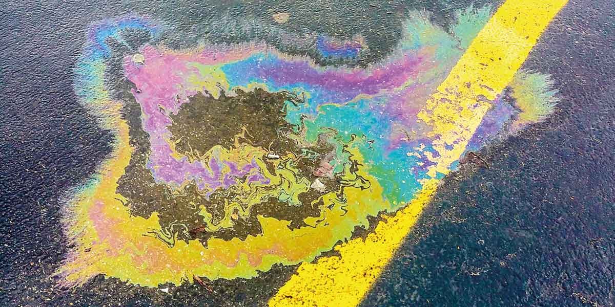 Colorful oil spill on black asphalt with a yellow painted line crossing diagonally.