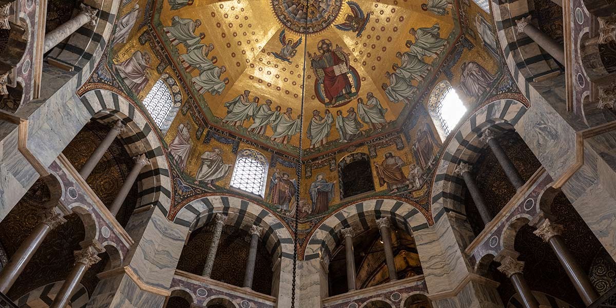 Ornate church ceiling with gold mosaics showing biblical figures and Jesus surrounded by arches and columns.