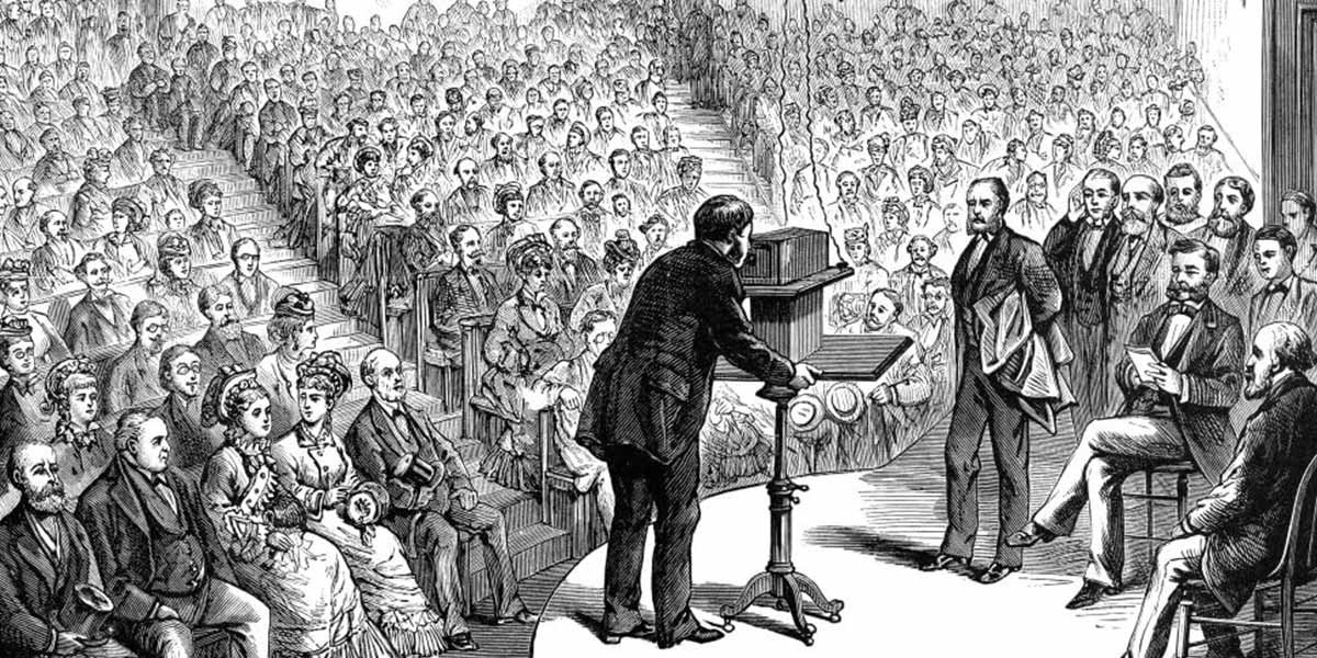 Black-and-white drawing of a man speaking to a large seated audience in a lecture hall.