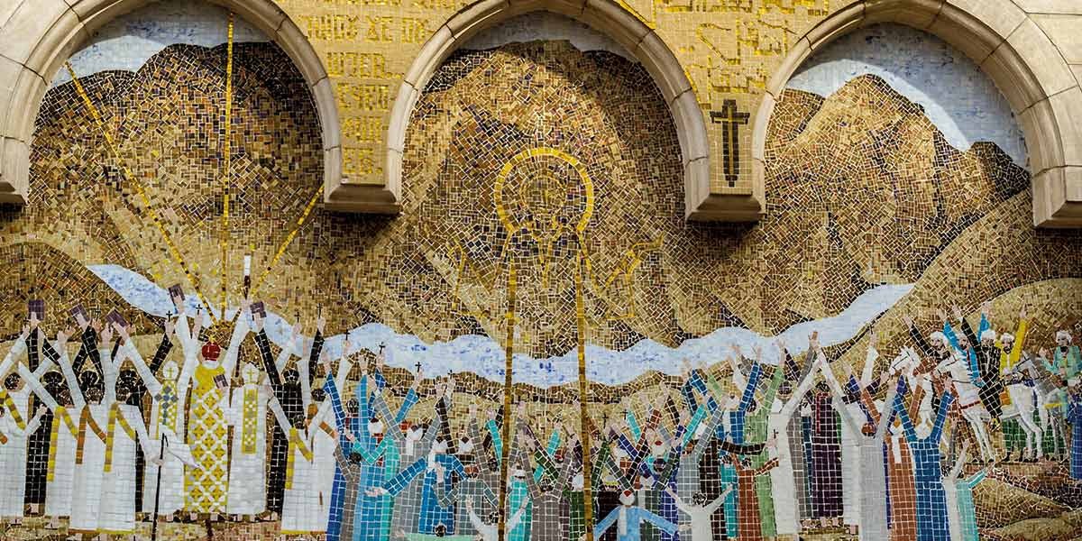 Mosaic art of religious figures with halos, crosses, and raised arms beneath stone arches and mountains.