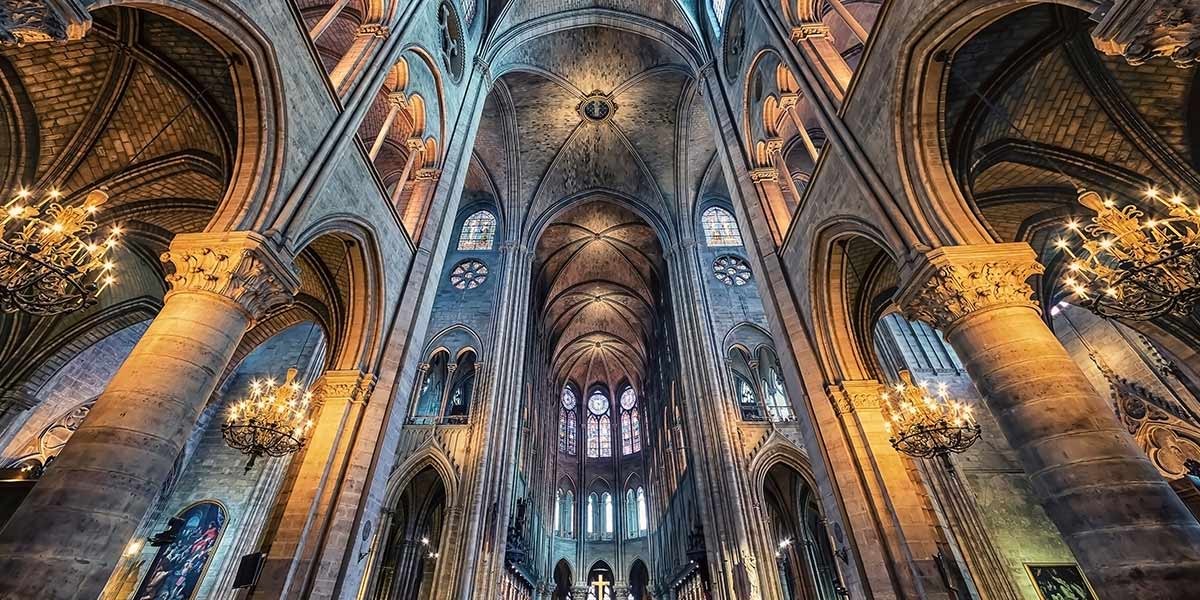 Interior of a gothic cathedral with tall arches, stained glass windows, and chandelier lighting.
