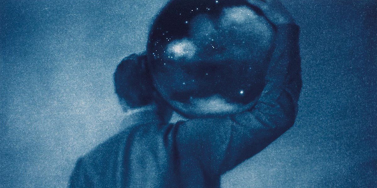 Figure holding a transparent sphere showing stars and clouds against a blue night sky.
