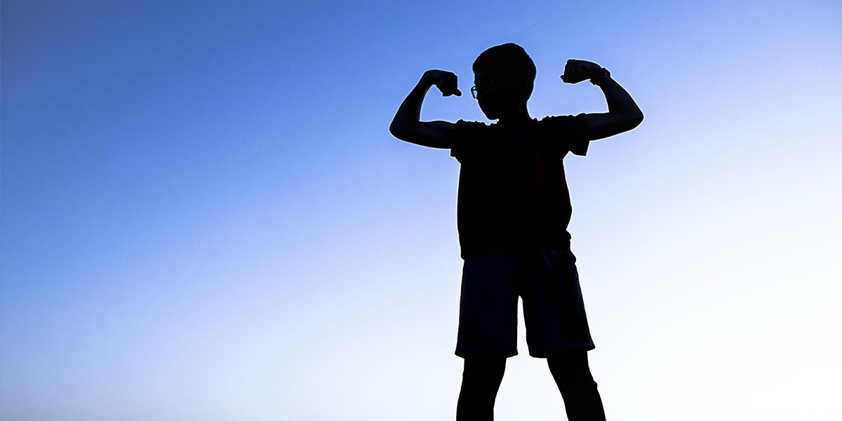 Silhouette of a child flexing both arms against a clear blue sky background.