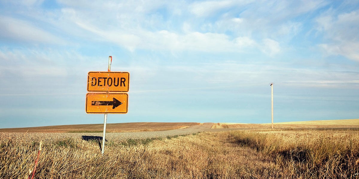 Orange detour road sign with right arrow in a rural field under a blue sky with scattered clouds.