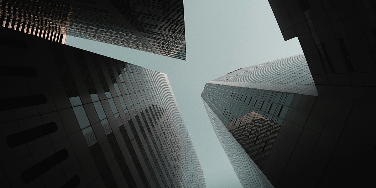 View looking up at four tall modern glass skyscrapers against a gray sky.