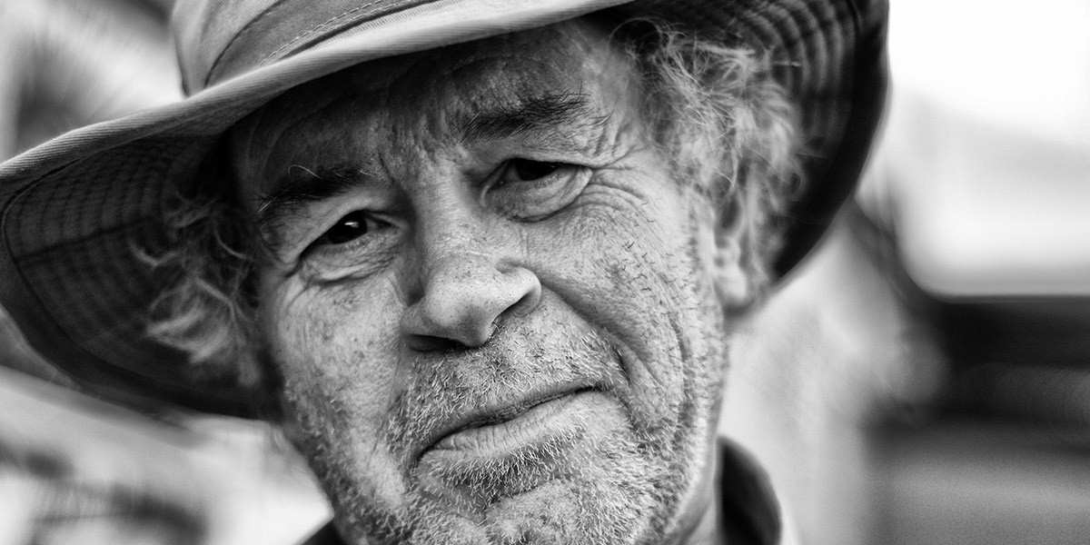Close-up black-and-white photo of an elderly man with a beard wearing a wide-brimmed hat.