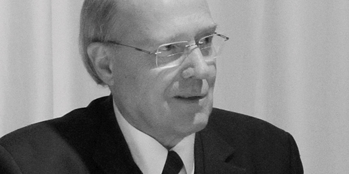 Black and white close-up of an older man wearing glasses, suit, and tie looking to the side.