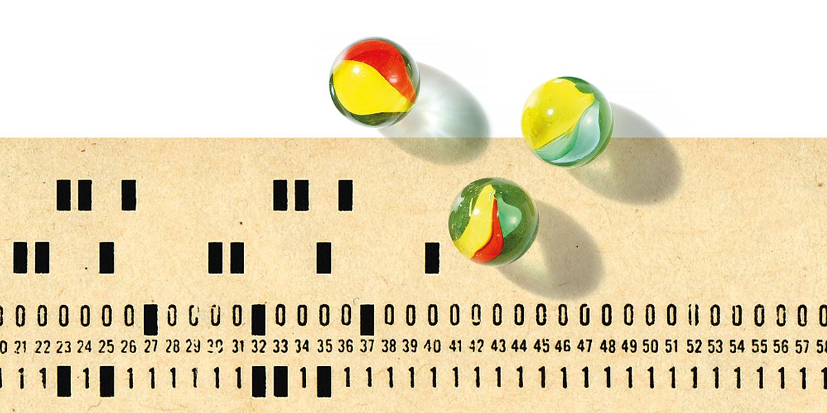 Three colorful glass marbles casting shadows on a vintage punched card with numbers and holes.