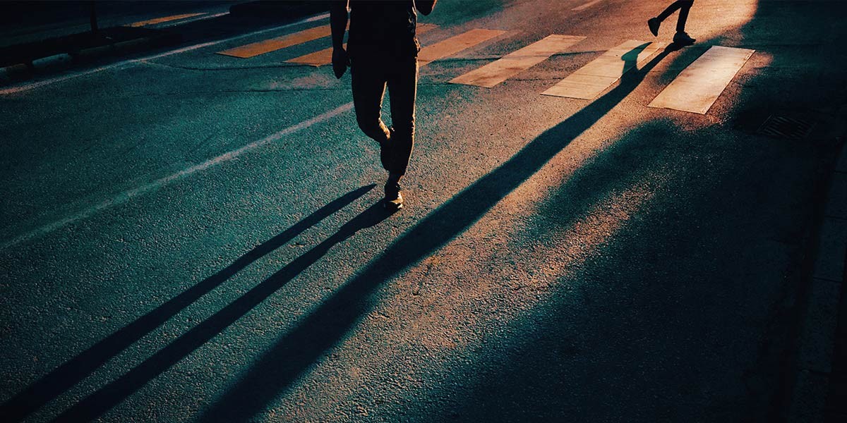 Two people crossing a street at a crosswalk casting long shadows in low sunlight.