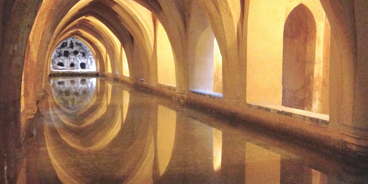 Arched hallway with yellow lights reflected in still water along the corridor.