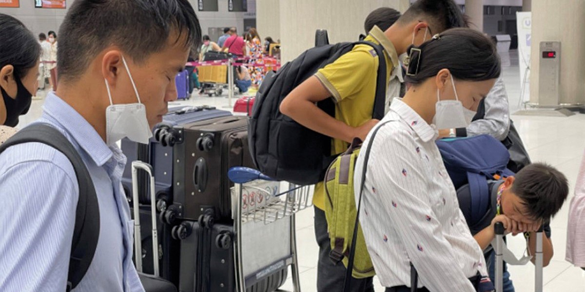 People wearing face masks standing with suitcases and backpacks in an airport terminal.