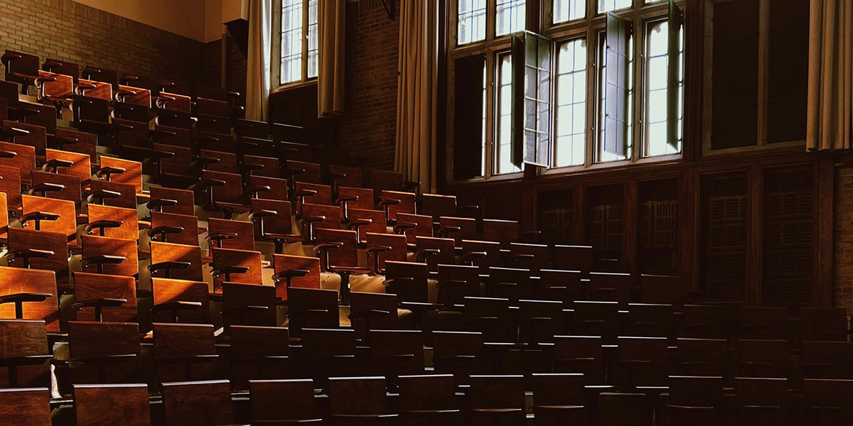 Sunlight shining through tall windows onto empty wooden seats in a classic lecture hall.