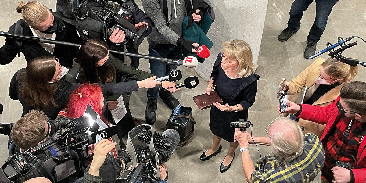 Woman holding a Bible surrounded by reporters and cameramen with microphones and cameras.