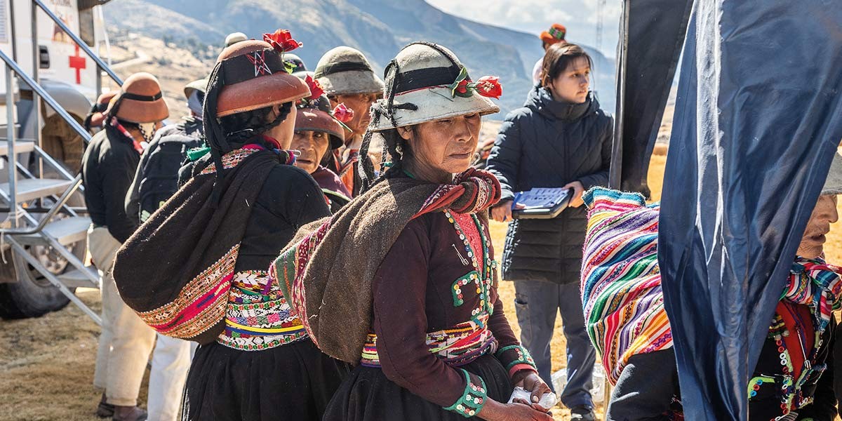 Group of indigenous women wearing traditional colorful clothing and hats outdoors near ambulance.