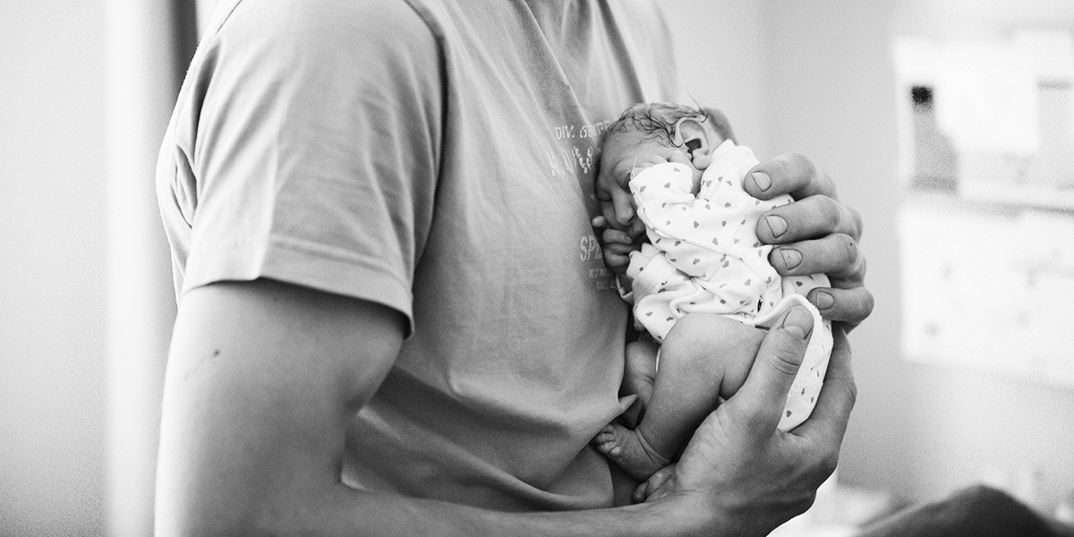 Black and white photo of a person cradling a sleeping newborn baby close to their chest.