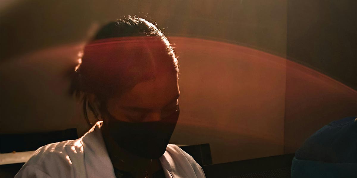 Person wearing a black mask with hair tied back and warm light shining across the face.