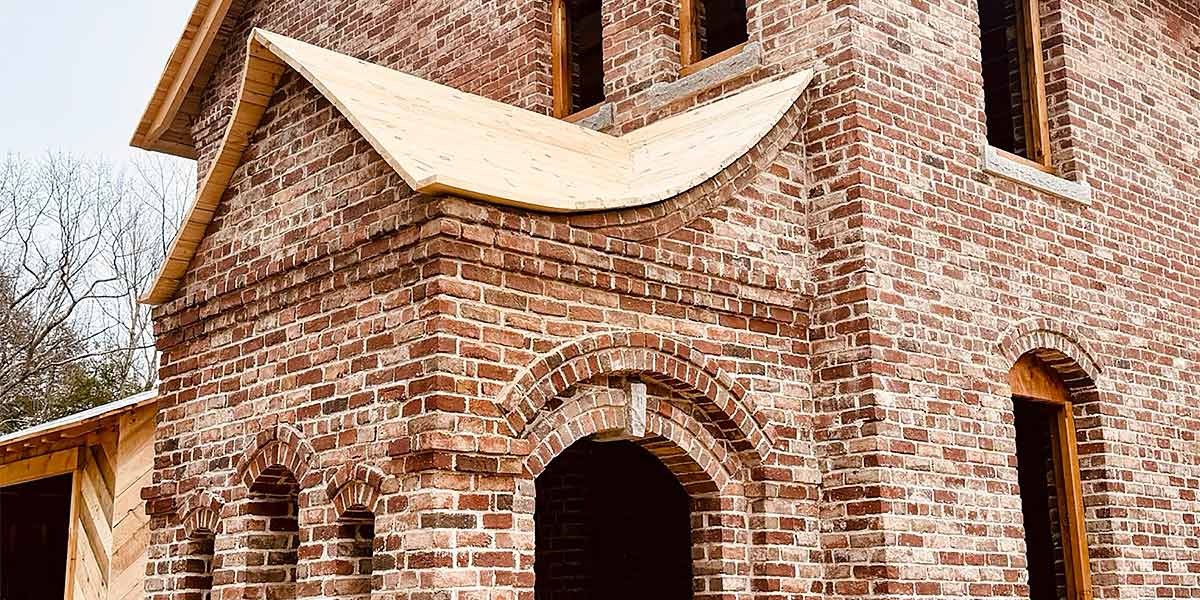 Partial view of a rustic brick building with unique curved wooden roof features and arched windows.
