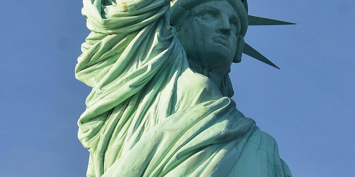 Close-up of the Statue of Liberty's face and raised arm against a clear blue sky.