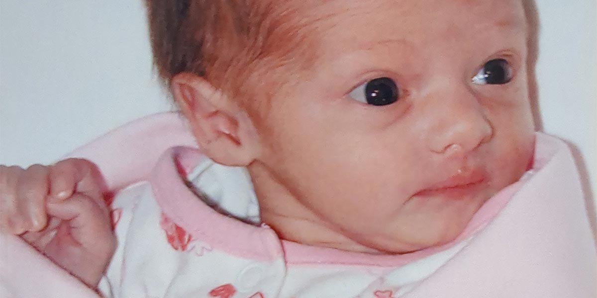 Close-up of a newborn baby wrapped in pink clothing looking to the right.