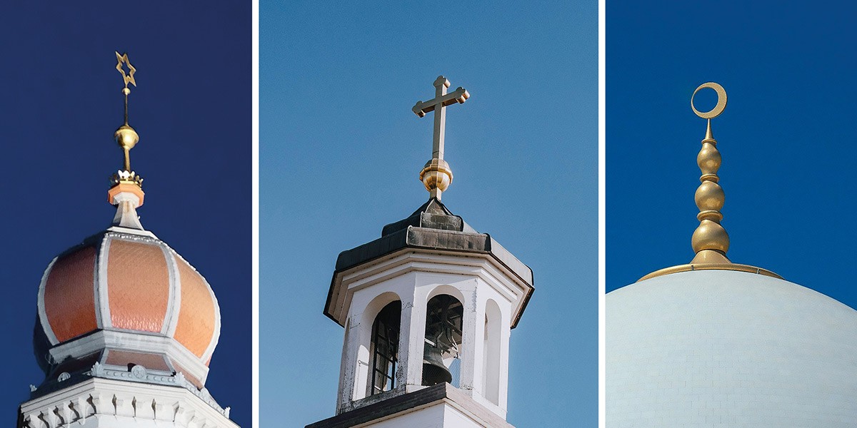 Three religious dome tops with symbols: Star of David, Christian cross, and Islamic crescent against blue sky.