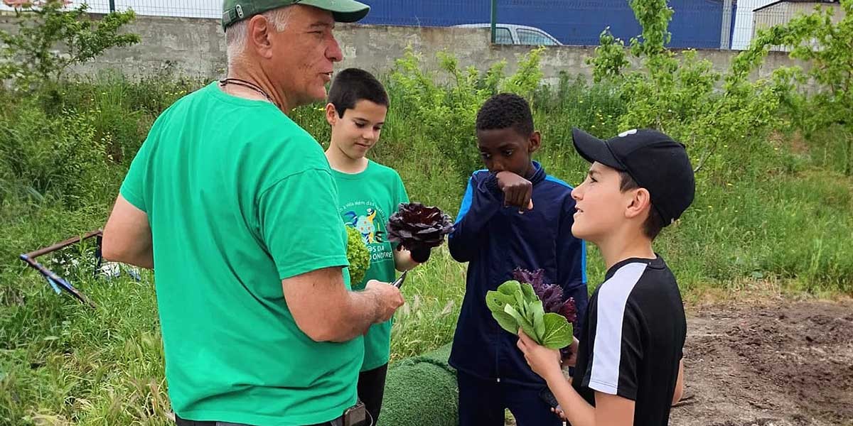 Man and three boys holding leafy greens outdoors in a garden or farm setting.