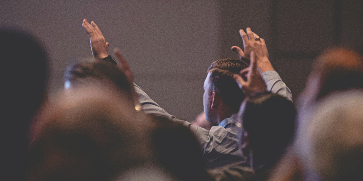 Man raising both hands in a crowd during an event or gathering indoors.