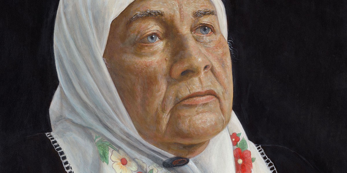 Close-up of an older woman with blue eyes wearing a white headscarf with embroidered flowers.