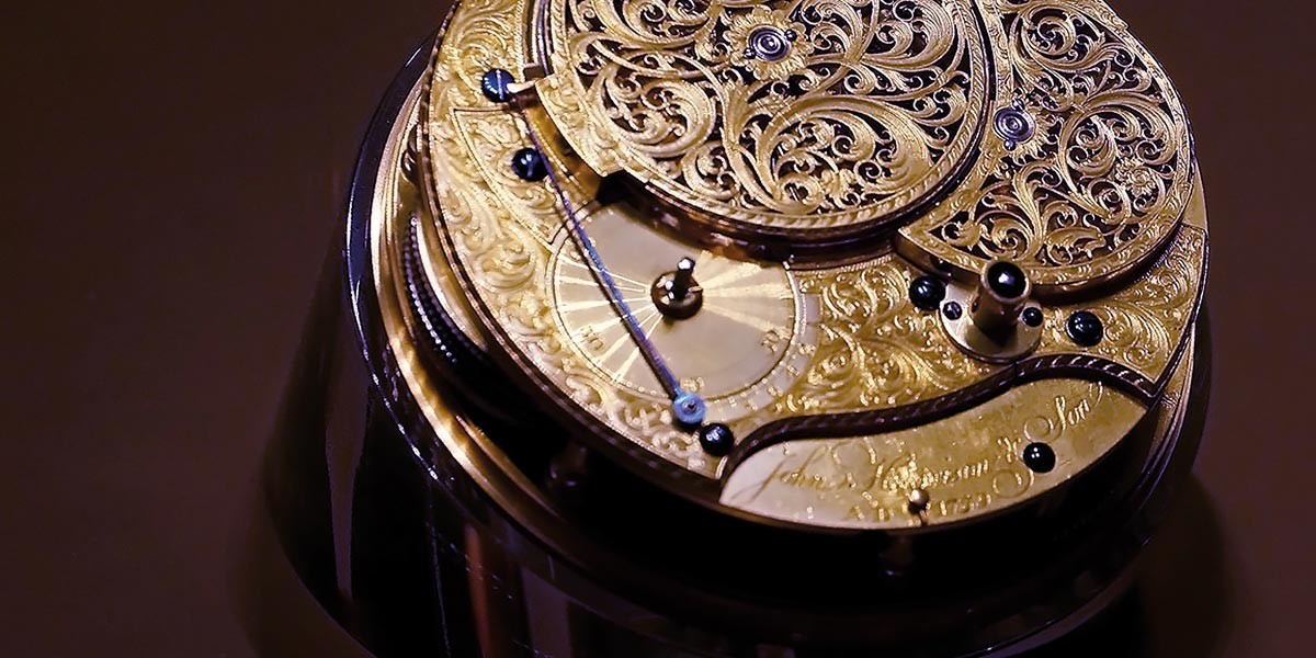 Close-up of an ornate gold mechanical watch movement with intricate engravings and blue screws.