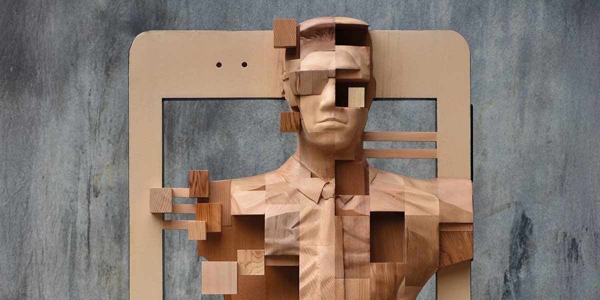 Wooden bust sculpture of a man with squares carved out creating a pixelated effect in front of a textured gray background.