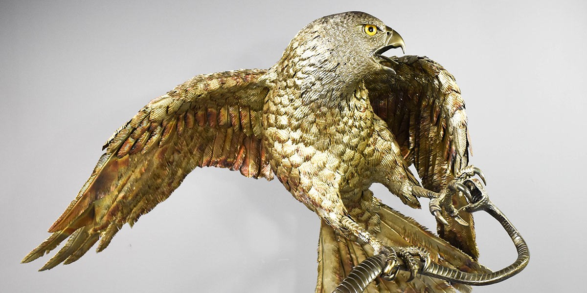 Detailed sculpture of a fierce hawk with wings spread and talons gripping a curved metallic object.