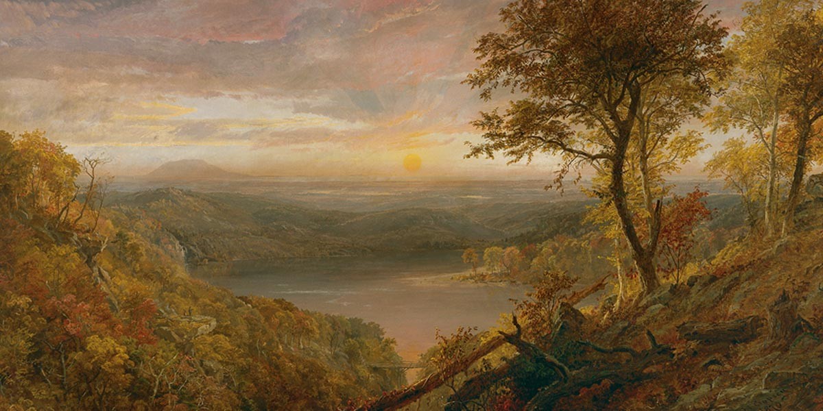 Autumn landscape with a lake surrounded by hills and trees under a cloudy sunset sky.