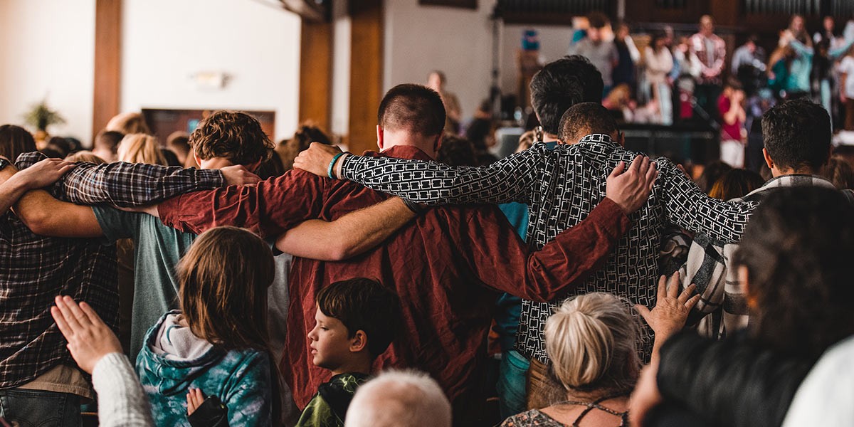 People standing close with arms around each other, in a supportive group gathering indoors.