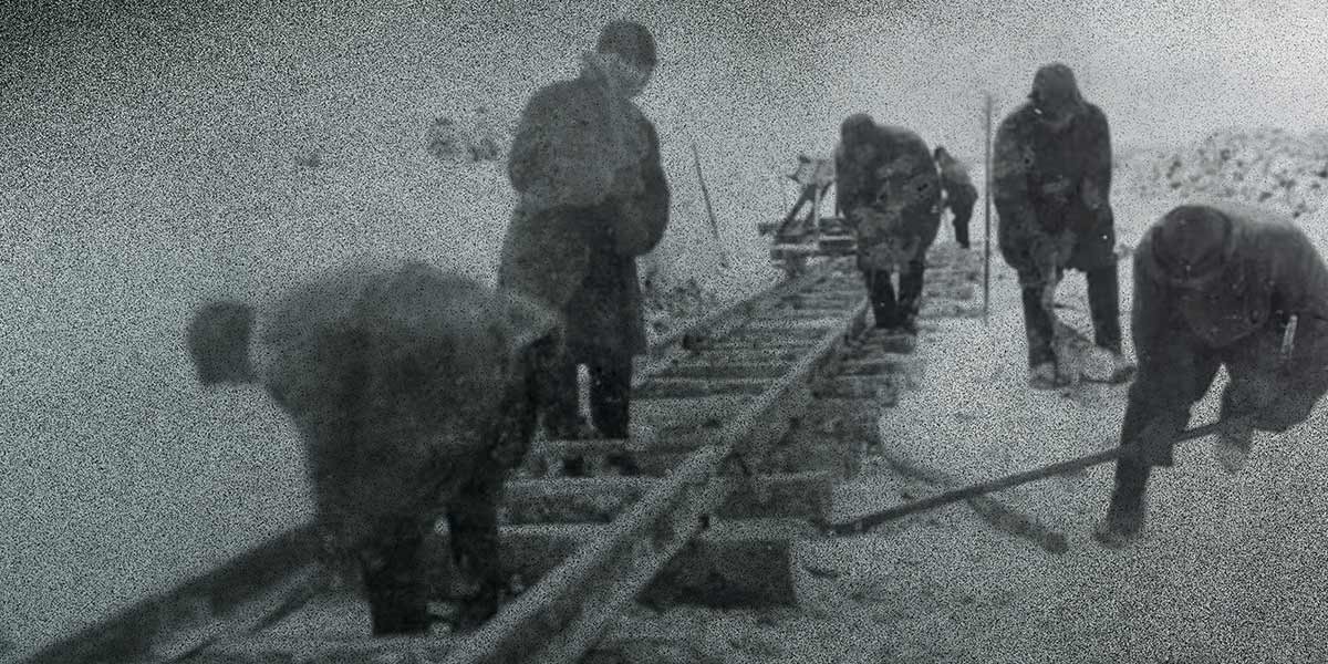 Black and white photo of six workers building a railroad track in snowy conditions.