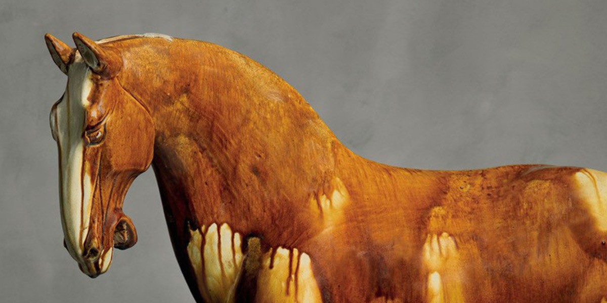 Brown horse sculpture with white dripping paint effect on its body against a gray background.