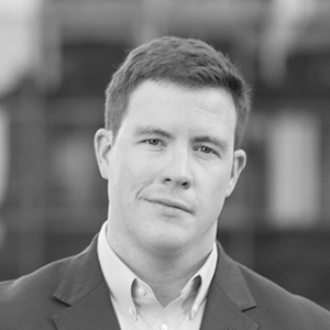 Black and white headshot of a man in a suit looking at the camera with a neutral expression.