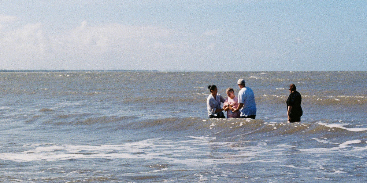 Four people standing waist-deep in ocean water under a cloudy blue sky.