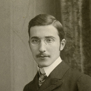 Portrait of a young man with glasses and a mustache wearing a suit and tie.