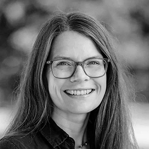 Smiling woman with long hair wearing glasses and a dark collared shirt.